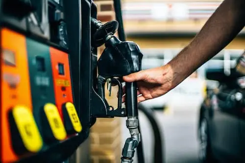 Hand holding a fuel nozzle at a gas station pump, ready to refuel a vehicle with regular gas.