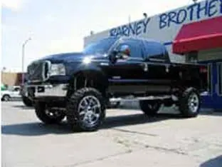 A black lifted pickup truck with shiny rims, one of the impressive customer rigs, parked outside a building with a "Barney Brothers" sign.