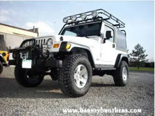 White off-road vehicle with roof rack and additional lights, parked on gravel. Check out this impressive example from our customer rigs at "www.barneybrothers.com.