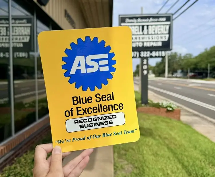 Harrell & Beverly Transmissions & Auto Repair in Sanford, FL holding the ASE Blue Seal of Excellence Recognized Business award in front of their shop