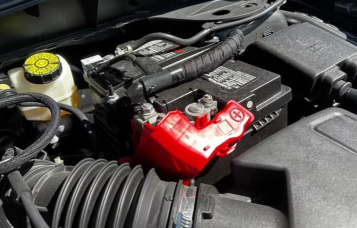 Car battery under the hood of a vehicle with the positive terminal cover visible, illustrating a blog about whether car batteries need to be registered after replacement.
