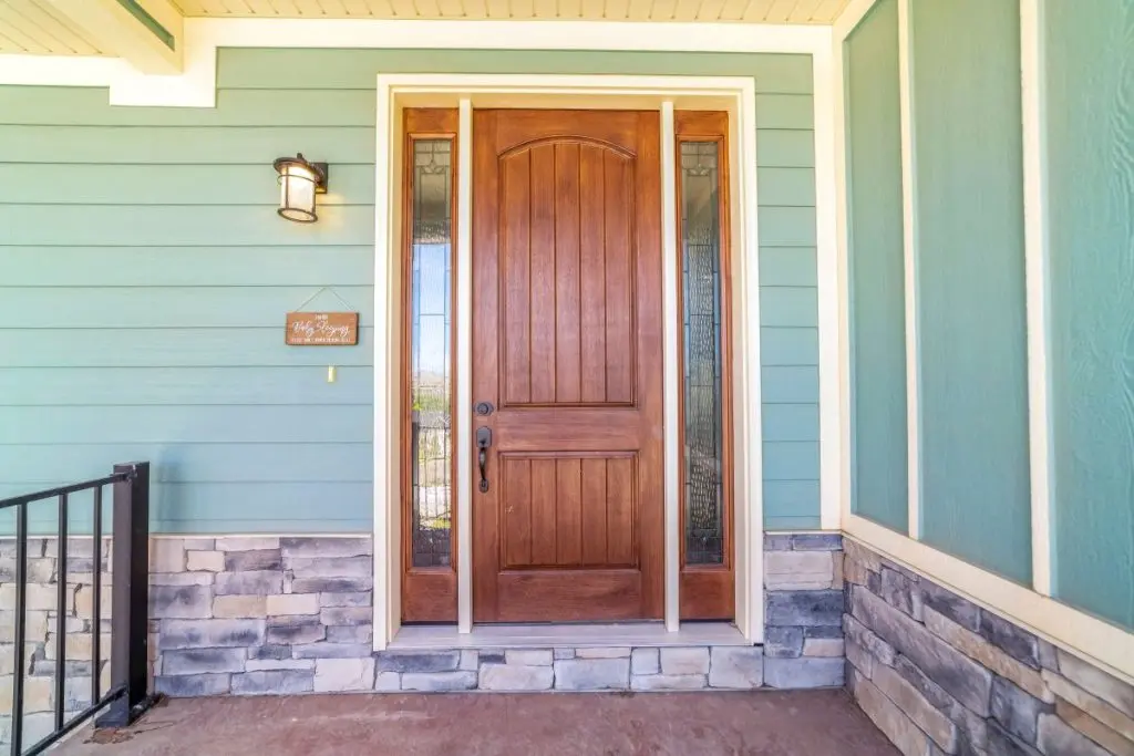 Front view of a home with green wall and brown wood door flanked by sidelights