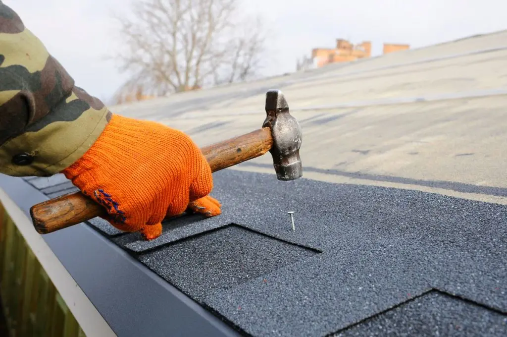 Builder Building Roof. Worker Hammer in Nails on the Roof.