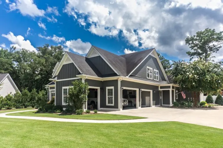 Roofing Saint Paul The side view of a large gray craftsman new construction house with a landscaped yard a three car garage and driveway.