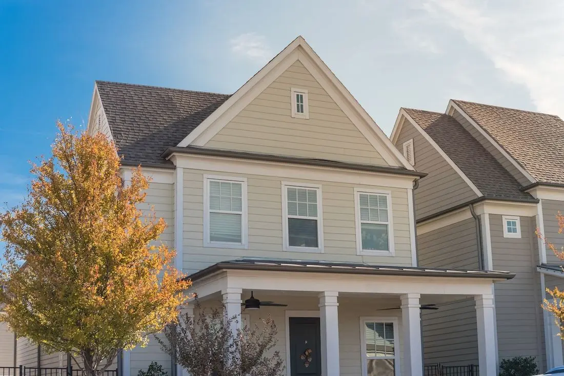 Upscale cottage style homes in suburbs Dallas, Texas with wood siding, covered porch patio with ceiling fans. Colorful autumn leaves and white cladding layer thermal insulation, weather resistance