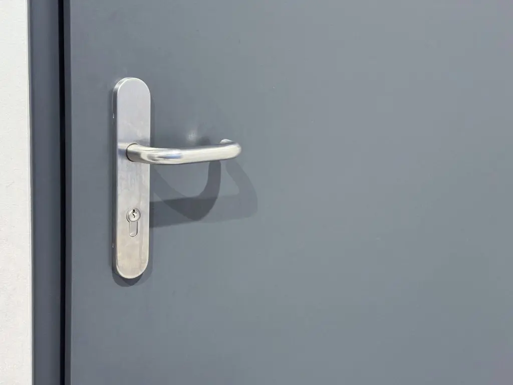A close-up view of a silver metallic door handle on a gray door with a minimalistic design and smooth surface