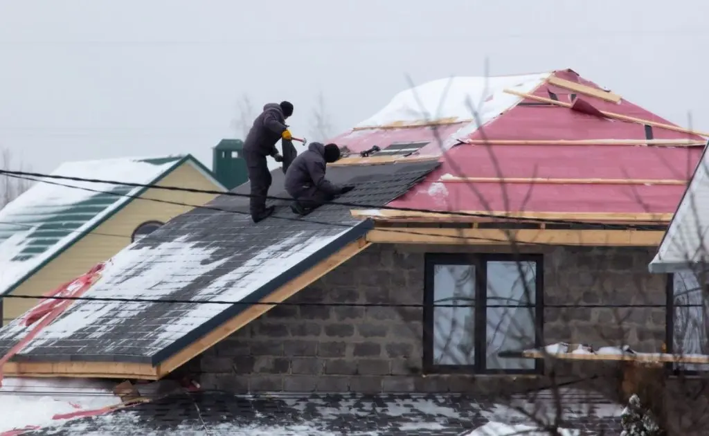 Workers install tiles on the roof of a house in winter
