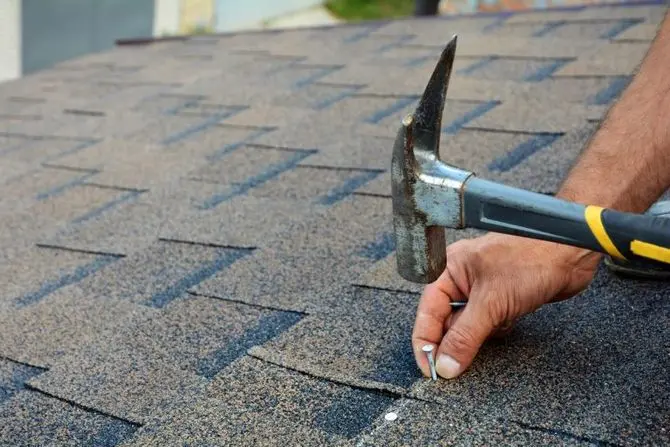 Roofer is hammering a Nail in the Roof Shingles