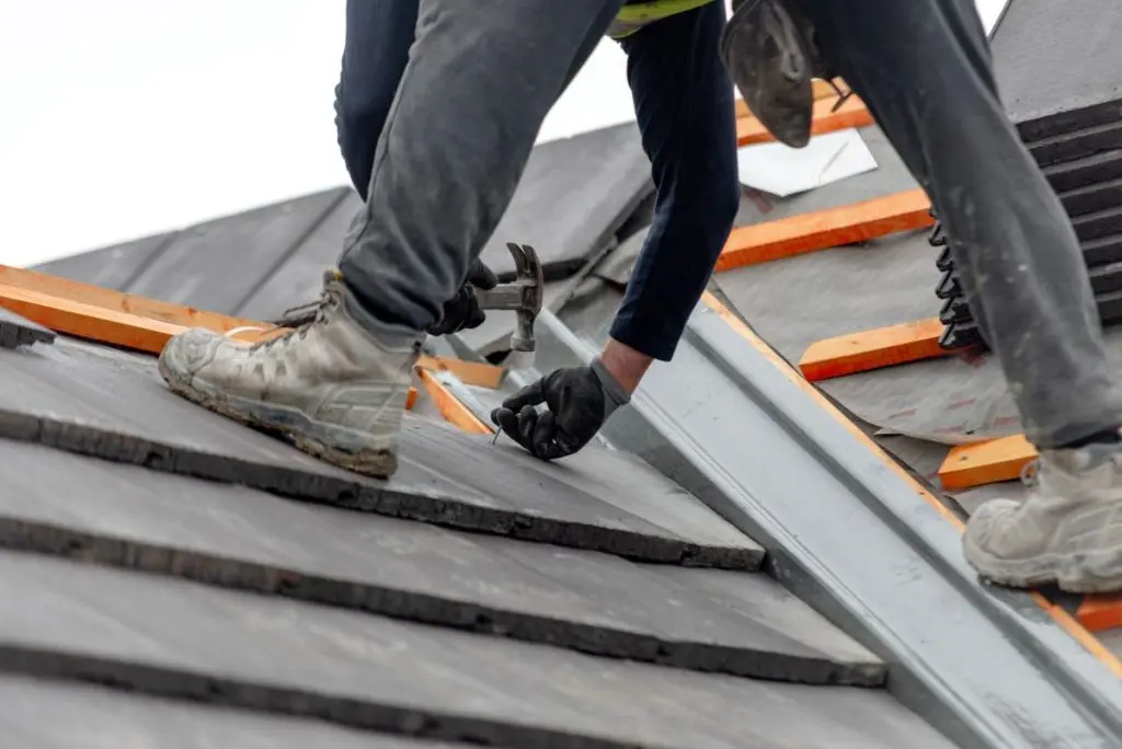 Construction worker carefully places roof tiles on a sloped surface while standing on top of a building