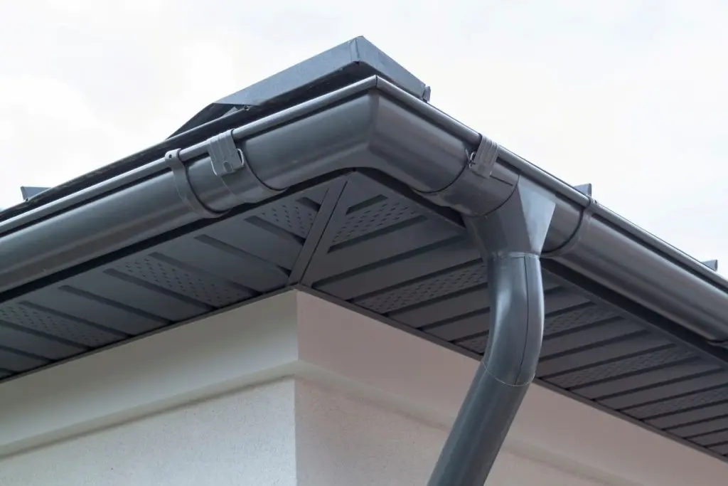 Corner of house with new gray metal tile roof and rain gutter