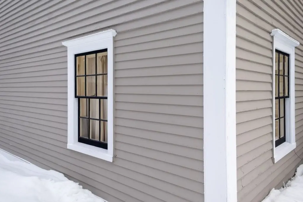 The exterior wall of the building is a beige clapboard. A snow drift is on the ground.