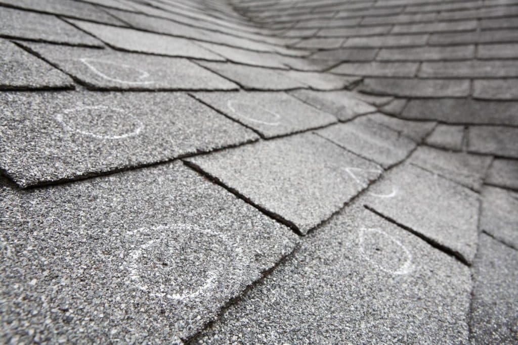 Old roof with hail damaged shingles, chalk circles mark the damage