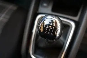 Close-up of a manual gear shift knob in a car, showing a six-speed pattern. The black and silver design conveys a sleek, modern feel.
