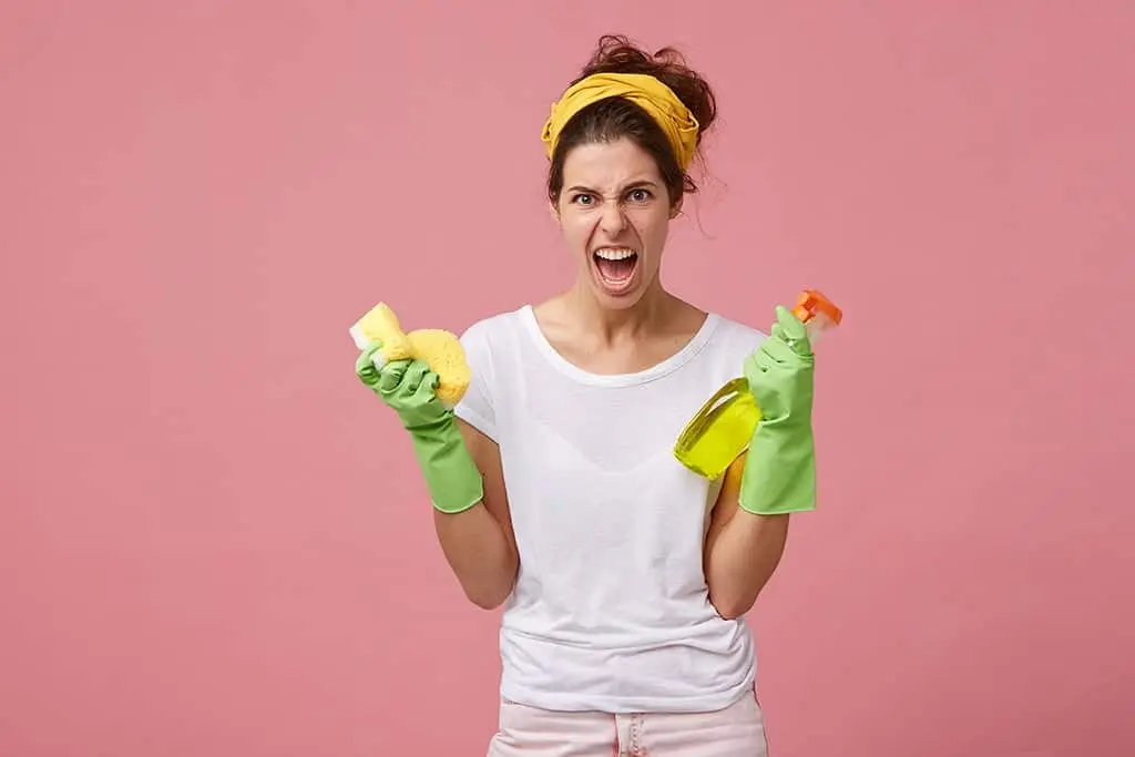 frustrated woman holding house cleaning supplies against a pink wall
