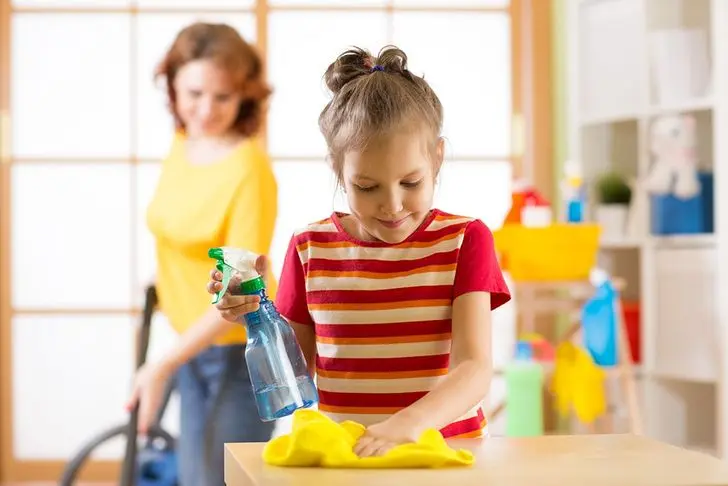 young girl doing house cleaning chores with mother mopping in background