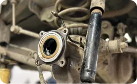 Close-up of a car suspension system showing an exposed wheel hub and shock absorber, with visible springs and suspension components covered in dirt and grime.
