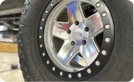 Close-up view of a shiny metal truck wheel rim with five spokes and a black tire featuring visible tread and small bolts around the rim’s edge.