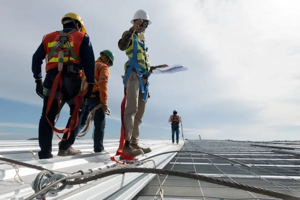 four workers performing commercial roof maintenance by inspecting a metal commercial roof