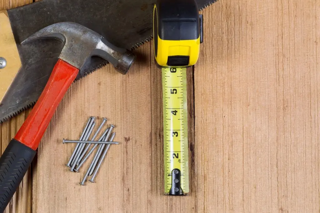 Top view of home repair tools consisting of wood saw, hammer, nails, and tape measure on cedar wooden shingles for roof