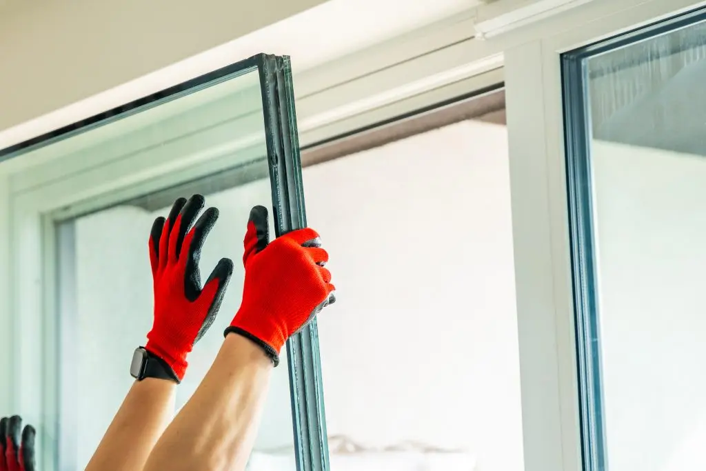 window installation cost Removed triple glazed window glass unit leaning near frame after replacement in apartment. Broken insulated glass panel removal and window repair process concept