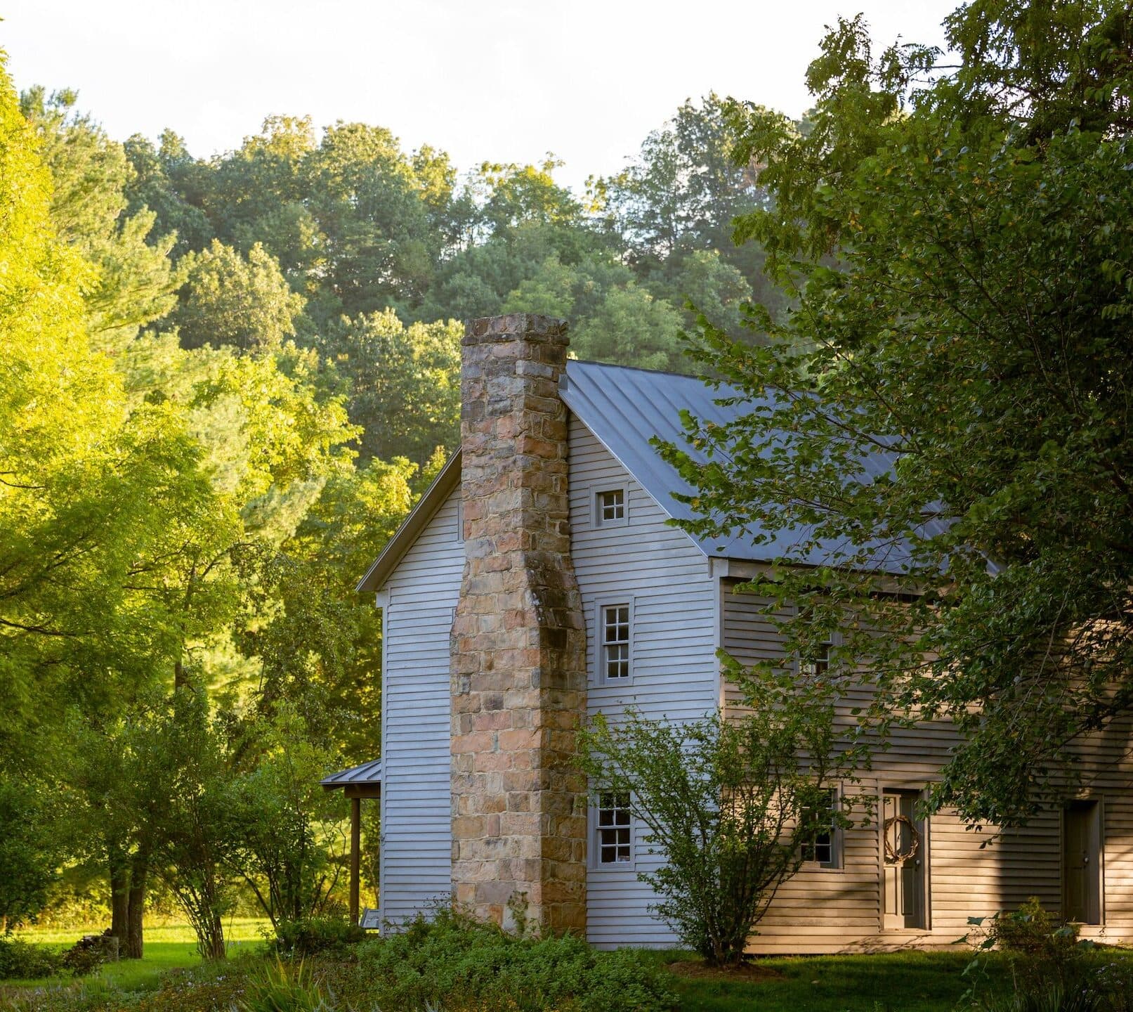 Old style grey colonial house with siding and metal roof in the woods