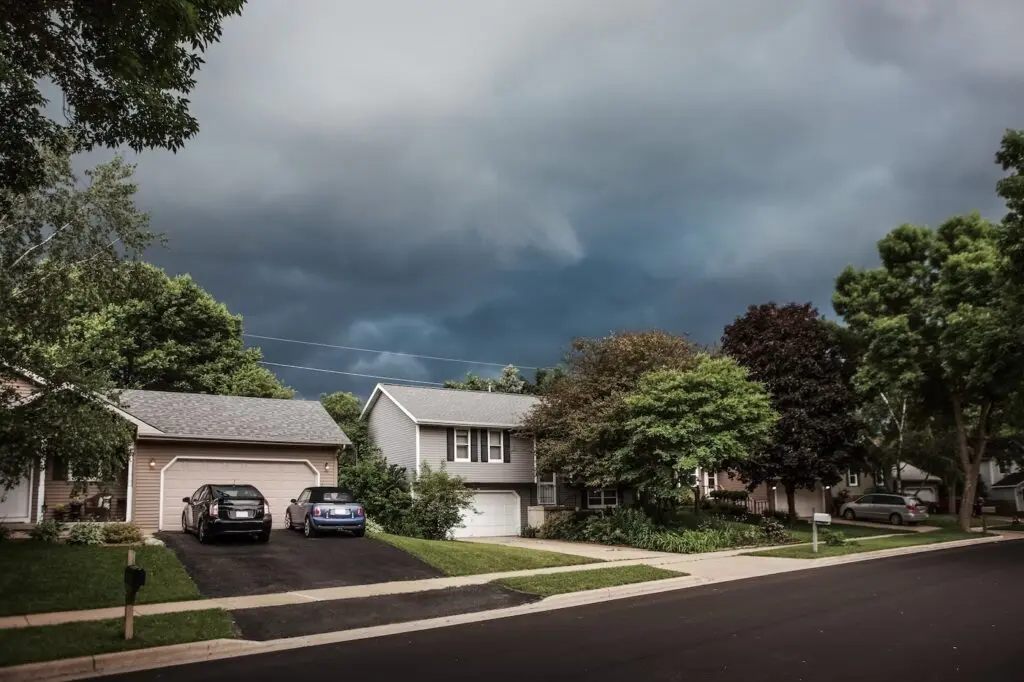 Dark storm clouds over suburban houses highlighting the need for storm damage roof replacement.