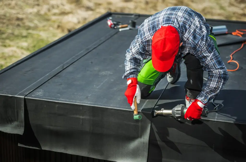 rubber roofing EPDM Membrane Installation on Top of a Garden Shed. Professional Worker Attaching Pieces of Material Using air Blower.