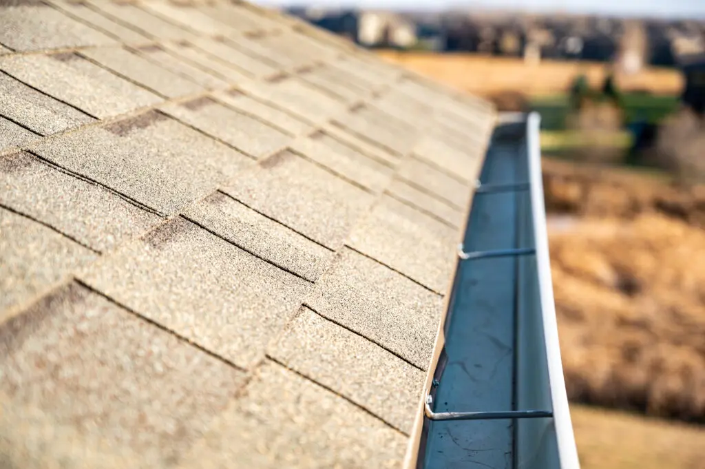 View from above looking down the edge of a roof gutter with clips and edge of shingles gutter sizes
