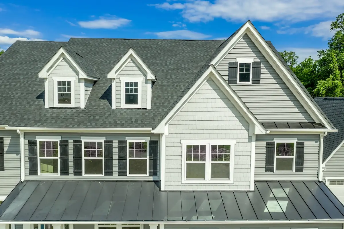 Classic American real estate single family home facade with horizontal vinyl siding, dormer windows, double gable, double and single sash windows, blue cloudy background