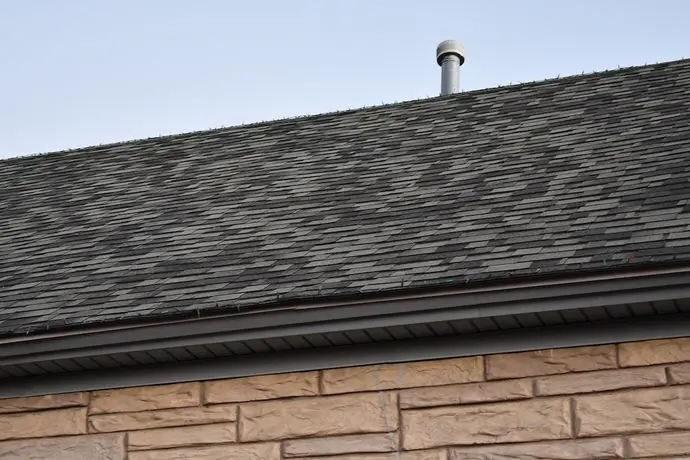 Standard 3 tab shingle roofing on classic stone structure. Small chimney vent on roof.