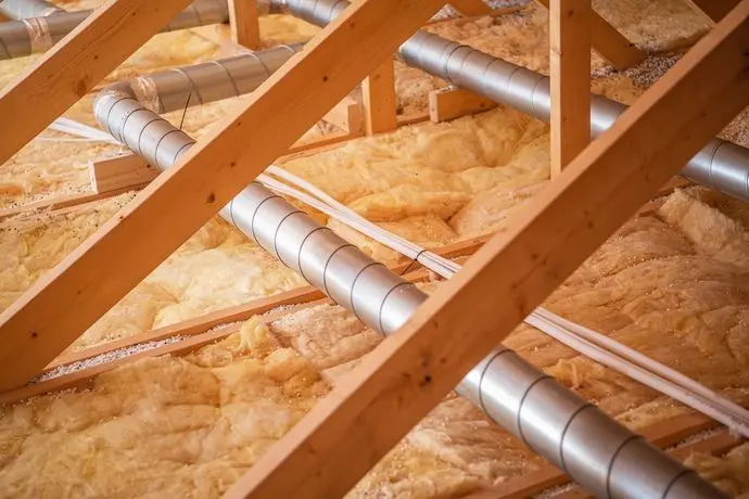 Wooden beams support a network of pipes and ductwork, showcasing insulation materials in a residential attic during ongoing construction activities.