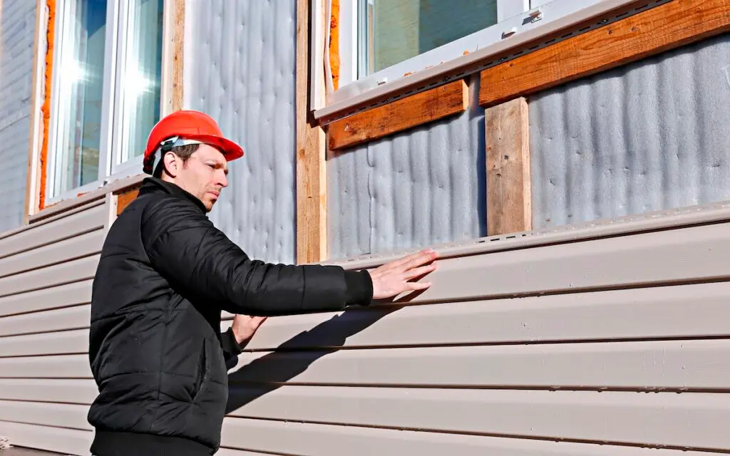 A worker installs panels beige siding on the facade. how to install vinyl siding