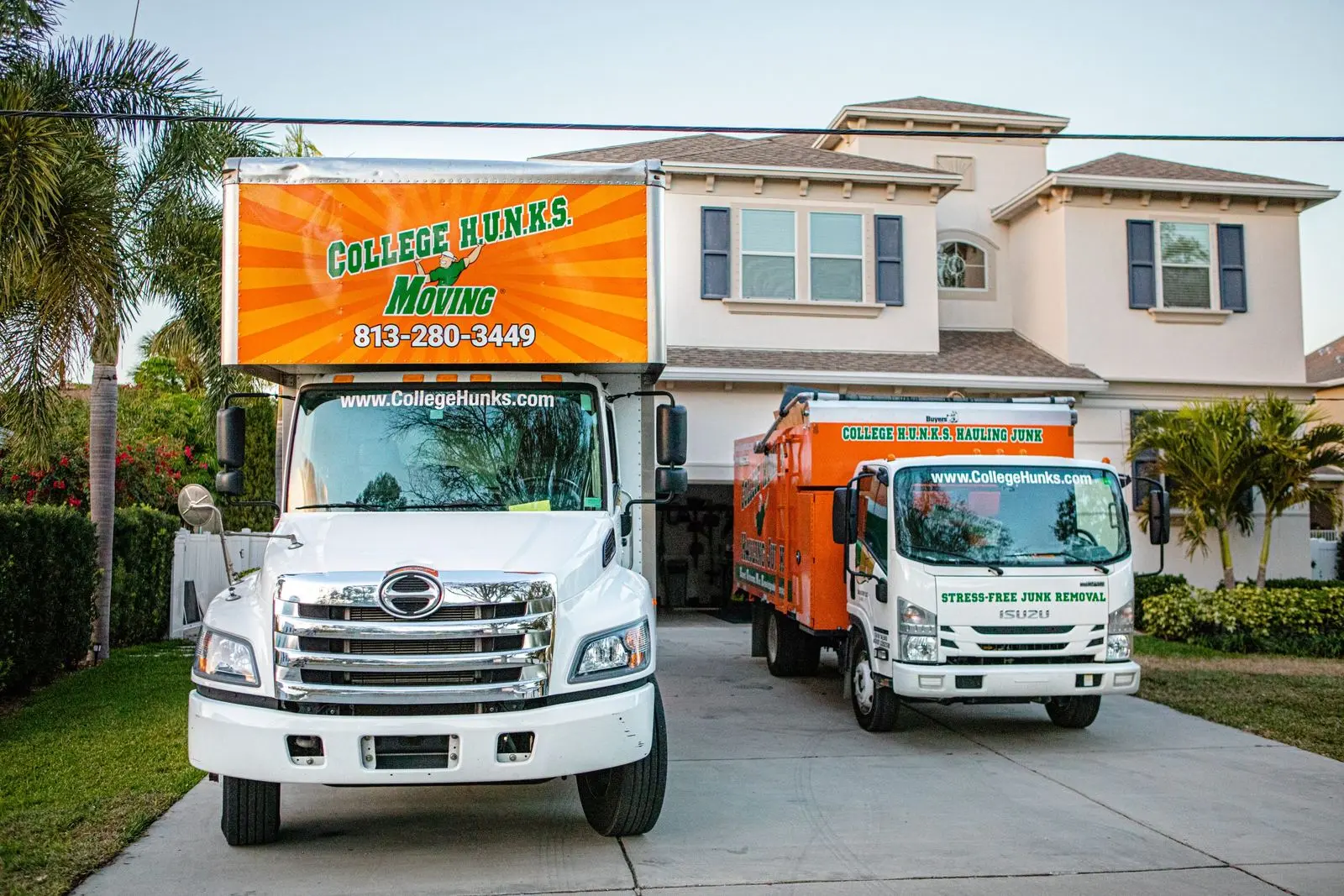 Two branded College HUNKS trucks in a driveway, the brand name on each cab, what a strong junk removal business name becomes