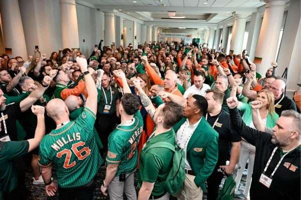 College HUNKS franchisees in green and orange team jerseys cheering with raised fists at a conference