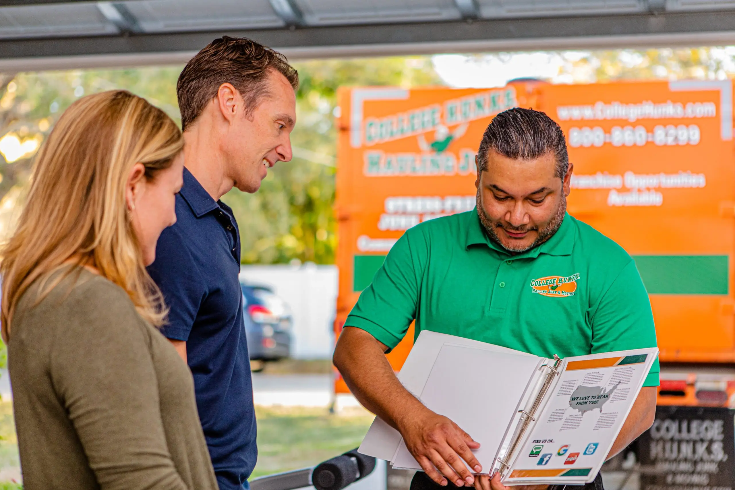 College HUNKS team member walking a couple through a binder next to a Franchise Opportunities Available truck