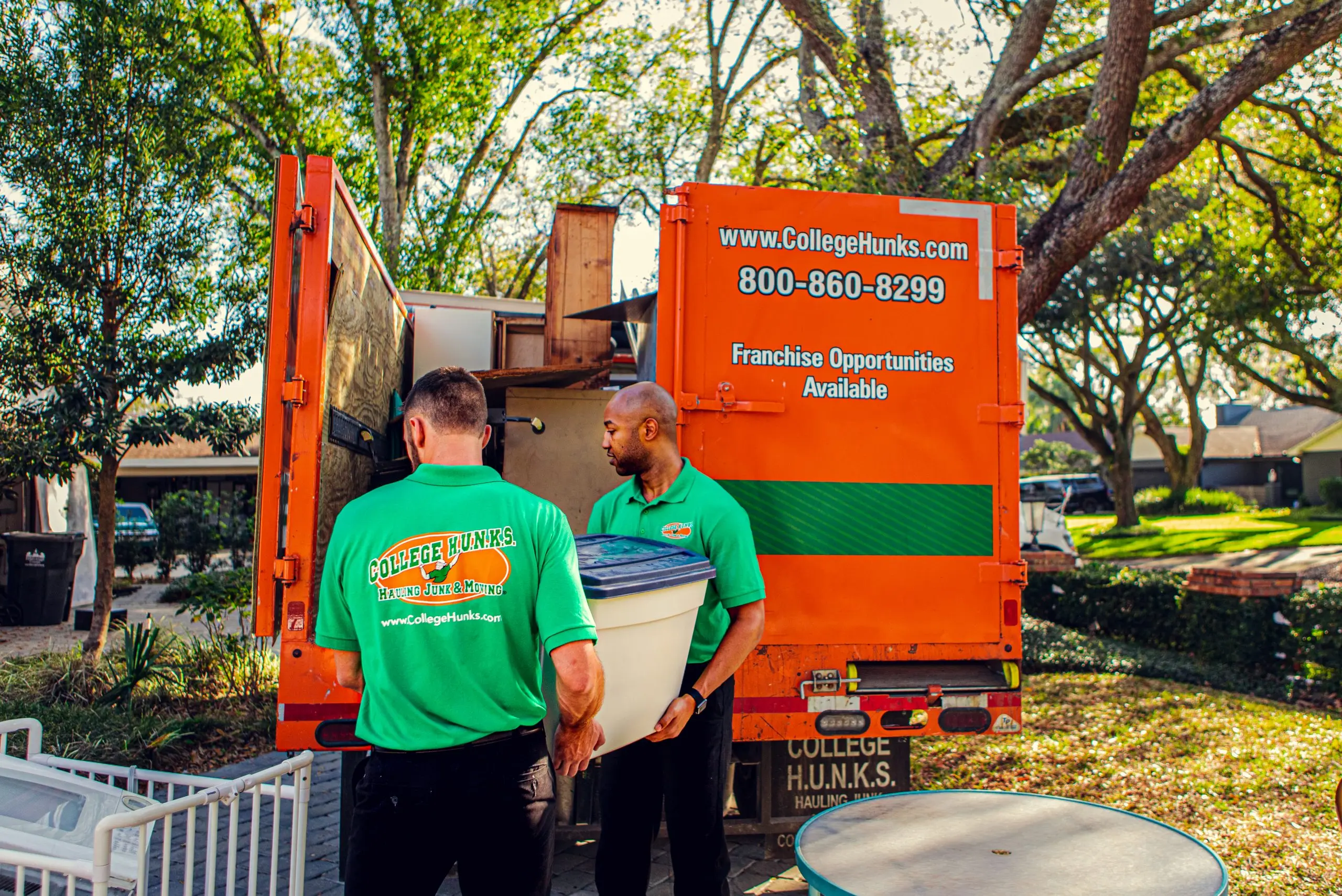 College HUNKS crew lifting heavy items into a junk removal truck at a customer's home