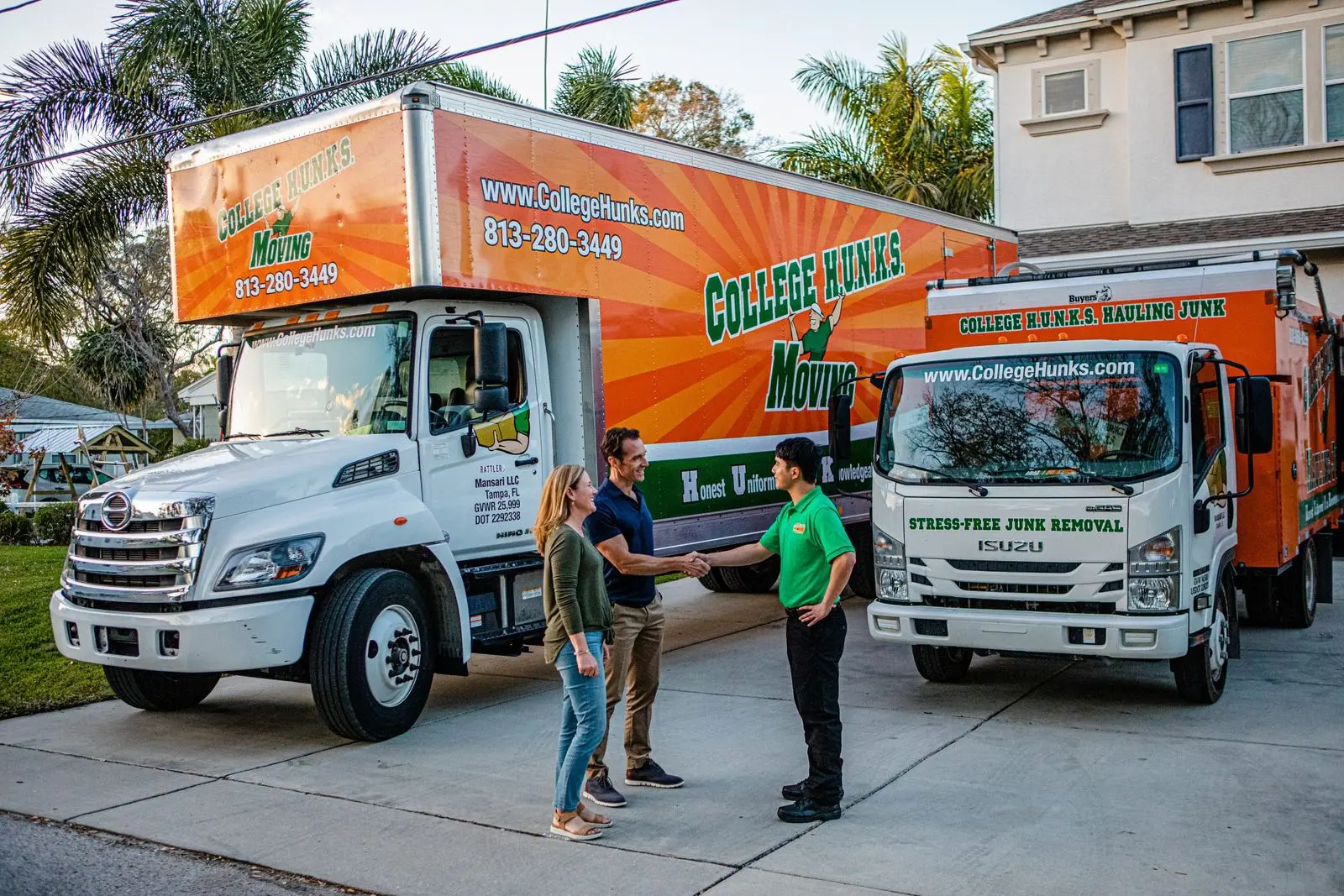 A College HUNKS crew member shaking hands with a homeowner couple in front of a moving truck and a junk removal truck, the two services one franchise territory runs