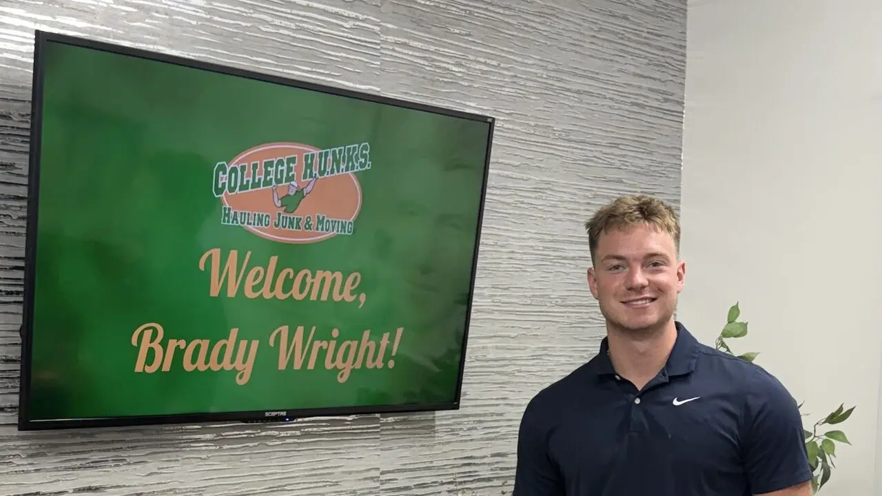 Brady Wright next to a Welcome, Brady Wright! screen at College HUNKS headquarters in Tampa