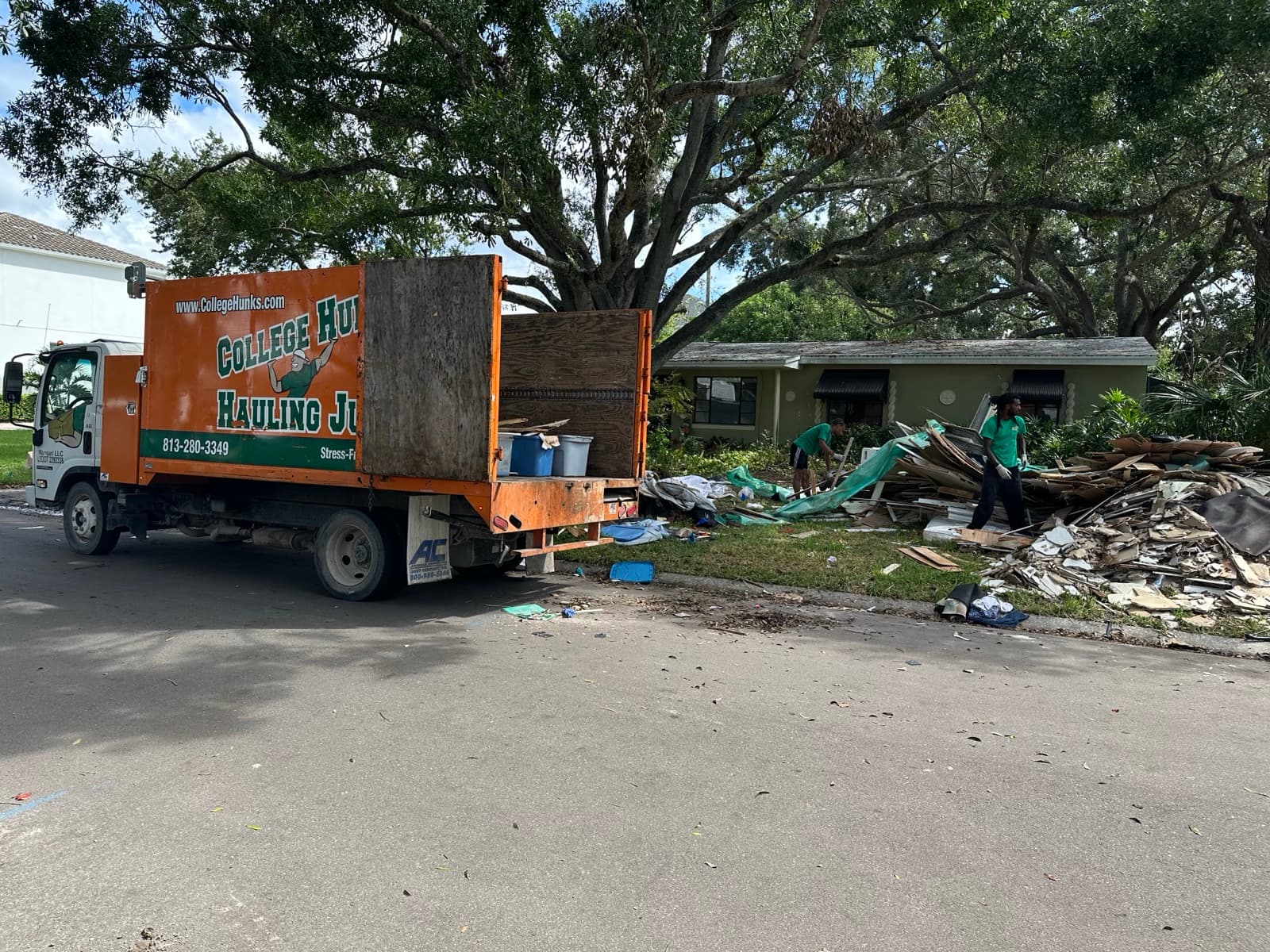 College HUNKS junk removal truck and crew clearing a large debris pile at a job site