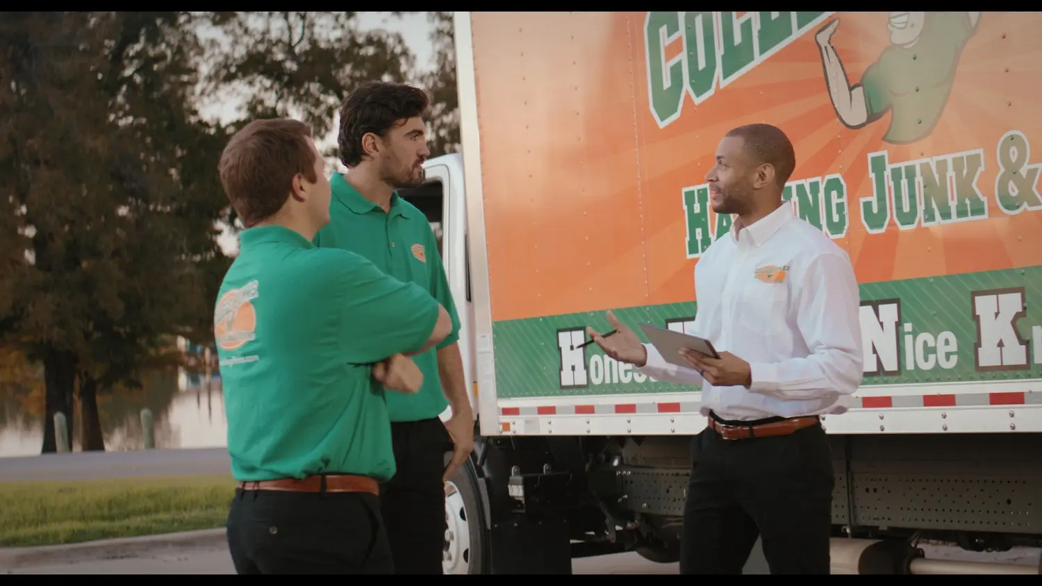 A College HUNKS franchise owner briefing two uniformed crew members beside a junk removal truck