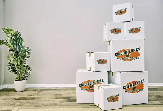 Stack of white College HUNKS branded moving boxes in an empty room
