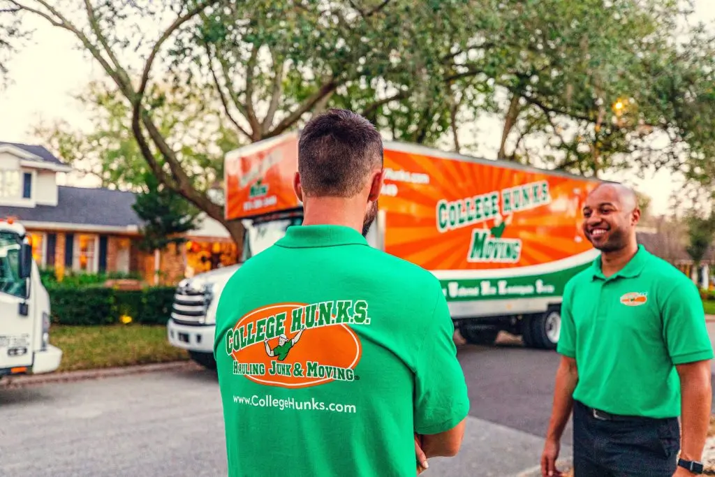 Two uniformed College HUNKS team members beside a branded College Hunks Moving truck outside a customer's home
