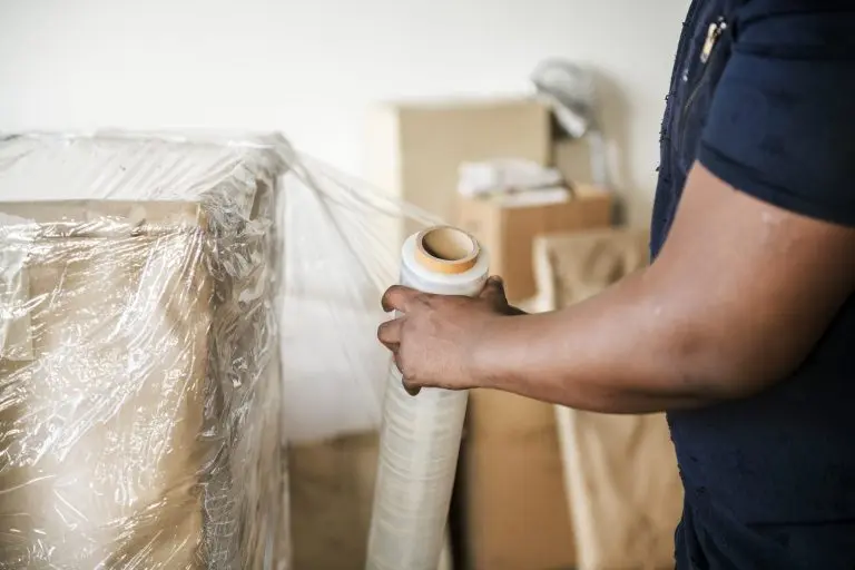 Mover shrink-wrapping furniture beside packed boxes, the kind of crew an independent moving company brings to a conversion franchise