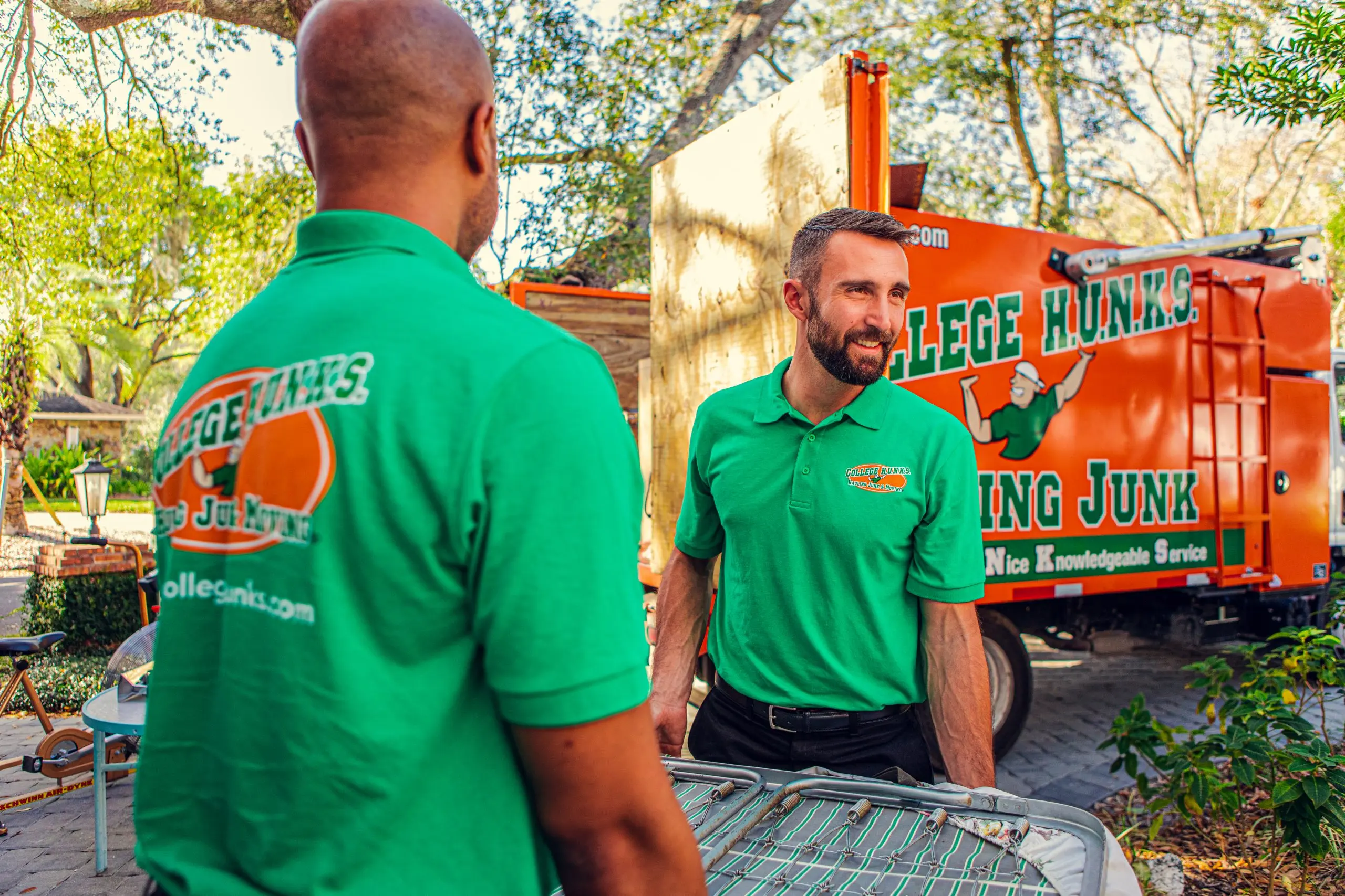 Two College HUNKS team members talking beside a branded junk removal truck