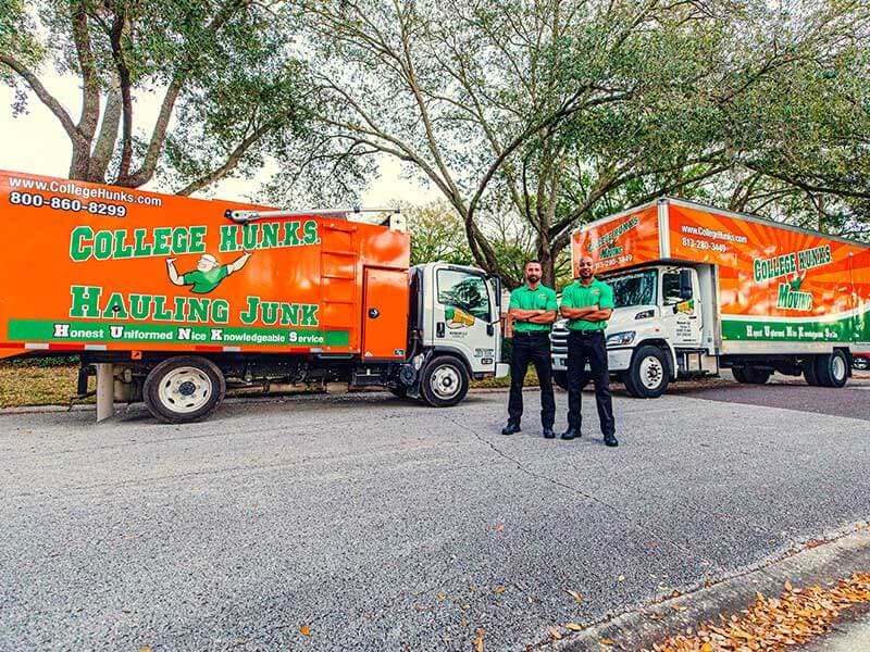 Two College HUNKS crew members in front of a junk truck and a moving truck