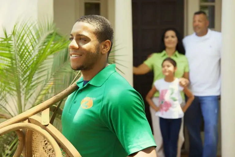 A uniformed College HUNKS mover carrying a chair past a family at their front door, the trust moving company marketing earns