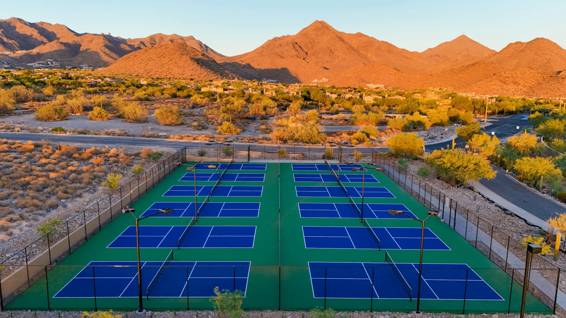 Aerial view of Village Clubs outdoor pickleball courts at DC Ranch, set in desert landscape with mountains at sunset.