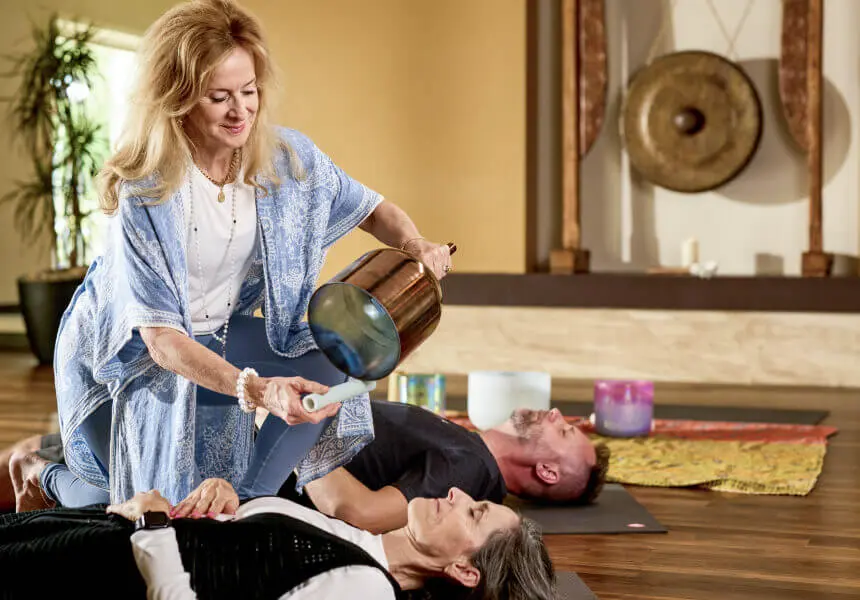 At Village Clubs Camelback, a woman uses a singing bowl in a sound healing and meditation session with yoga mats and crystal bowls.