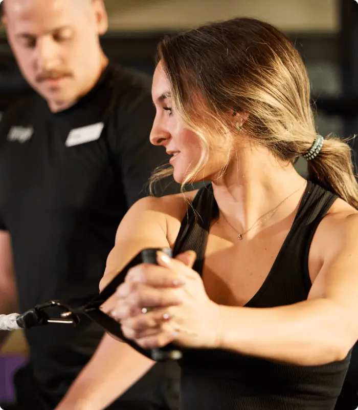 A woman trains with resistance bands at Village Clubs Camelback as a trainer in black offers guidance in the gym.