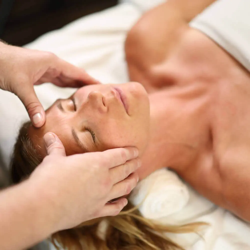 A guest enjoys a gentle facial massage at Village Clubs Camelback, relaxing on a massage table covered with a white towel.